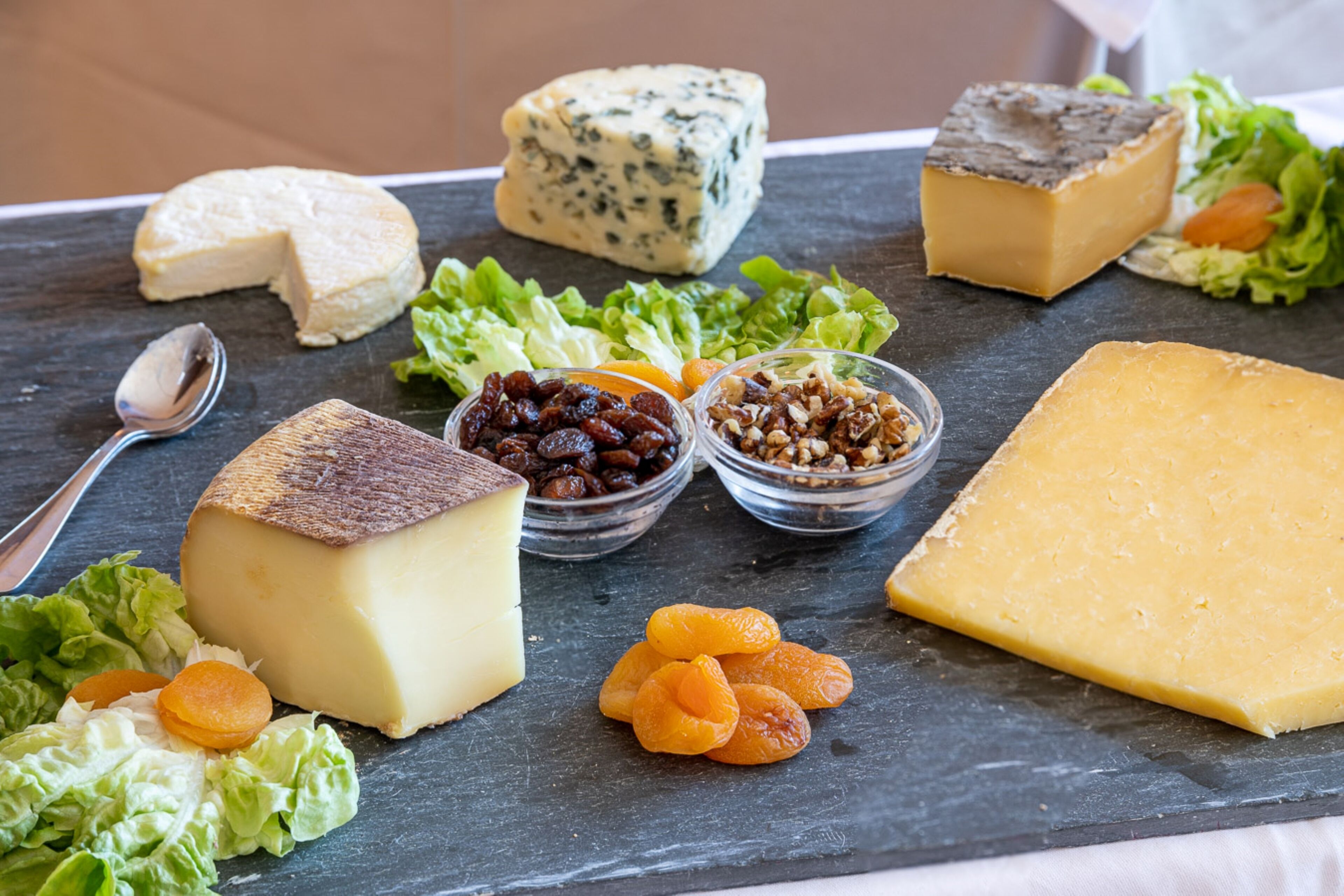 A variety of cheeses and nuts on a slate board.