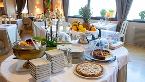 A breakfast buffet with various fruits, a large bowl of cereal, and a pie on a table in a well-lit dining area with a view of the outdoors. - Best Western Le Relais de Laguiole Hotel & Spa (Laguiole)