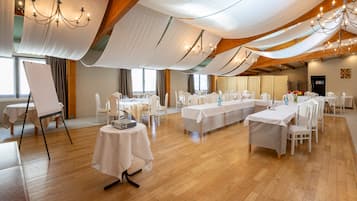 Une salle de banquet avec des tables et des chaises blanches, un plancher en bois et des rideaux blancs tombants.