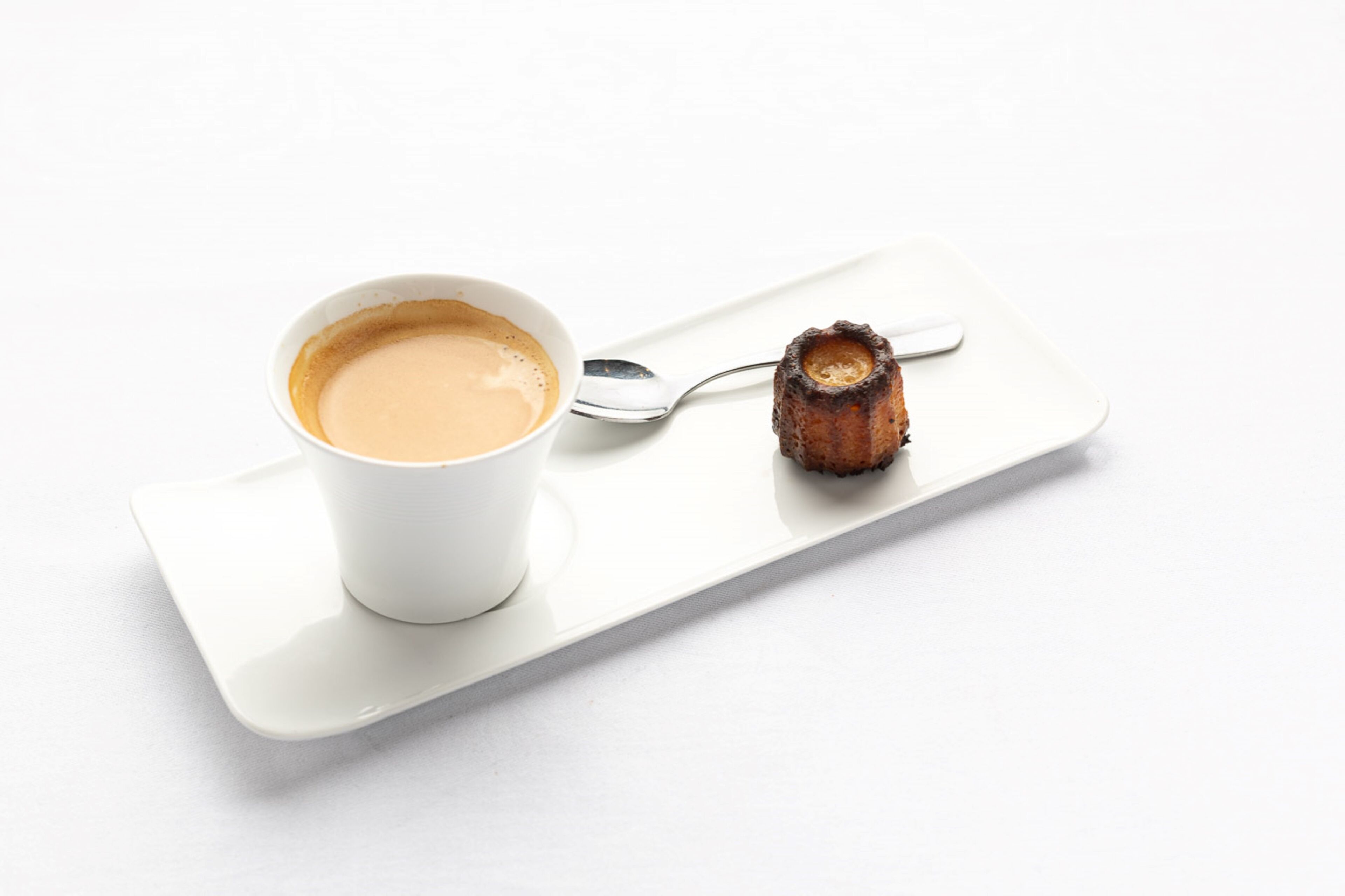 A white cup of coffee on a white tray with a spoon and a piece of burnt toast.