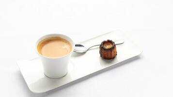 A white cup of coffee on a white tray with a spoon and a piece of burnt toast.