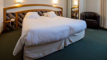 Una cama bien tendida con cabecera, una mesita de noche con lámpara y una silla en una habitación de hotel.