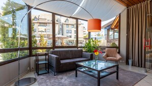 A modern living room with a glass coffee table, a sofa, and a chair. Large windows offer a view of buildings and trees. - Best Western Le Relais de Laguiole Hotel & Spa (Laguiole)