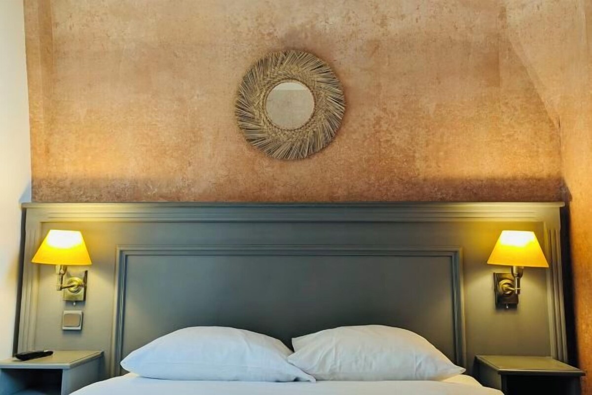 Habitación de hotel con una cama grande, dos lámparas de noche y un espejo montado en la pared.