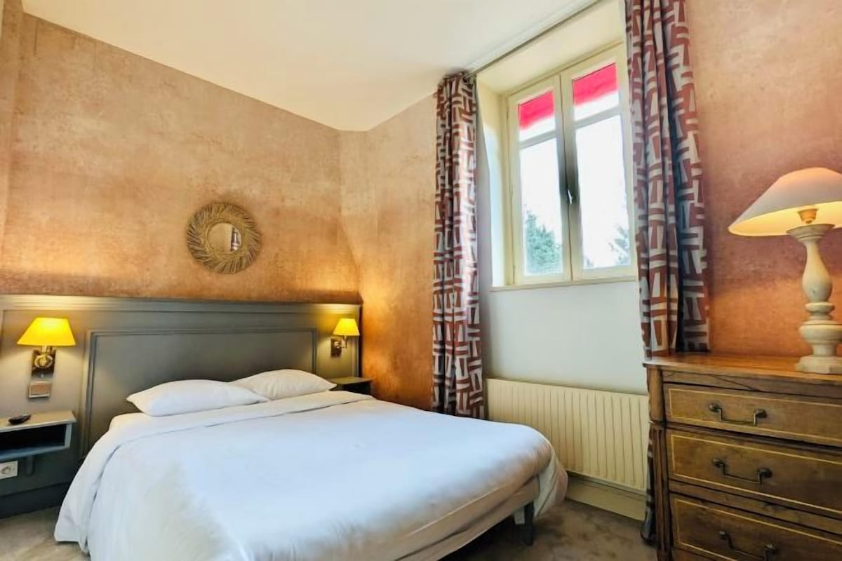 A hotel room with a bed, two bedside lamps, a dresser, and a window with curtains.
