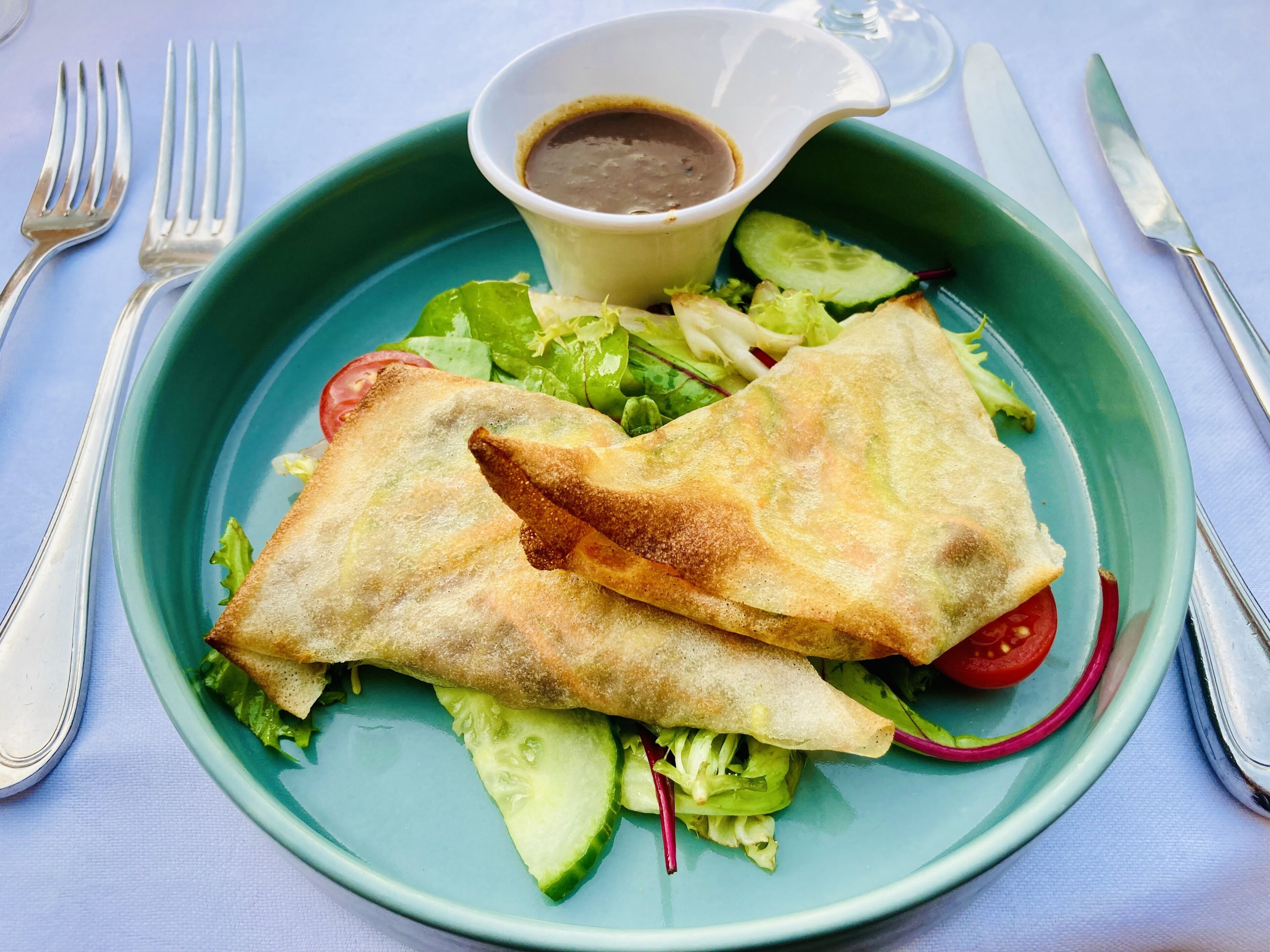 A plate with a salad, two folded items, and a small bowl of sauce.