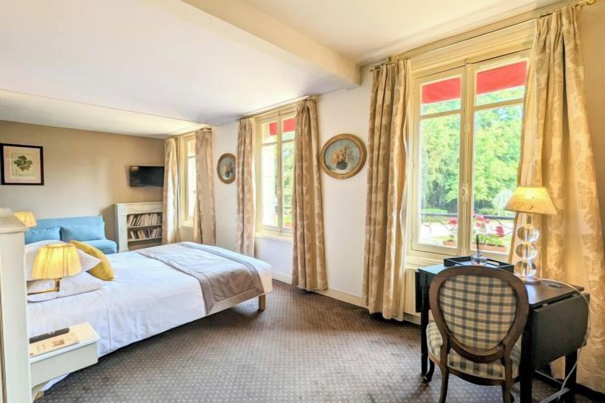 A bedroom with a bed, bedside table, lamp, chair, desk, and curtains.