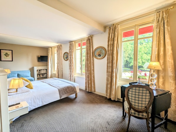 Habitación de hotel con cama, escritorio, silla, estantería y ventana con cortinas.