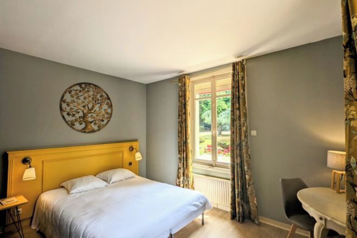 Un dormitorio con una cama, un adorno circular en la pared, una ventana con cortinas y una mesita de noche con lámpara.