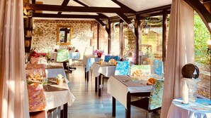 A covered outdoor dining area with tables set for guests, wooden beams, and brick walls. - Château Corneille (Le Val d'Hazey)