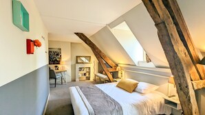 A bedroom with a sloped ceiling, a bed with white bedding, a desk with a chair, and a bookshelf. - Château Corneille (Le Val d'Hazey)