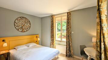 A bedroom with a bed, a round wall decoration, a window with curtains, and a small table with a chair.