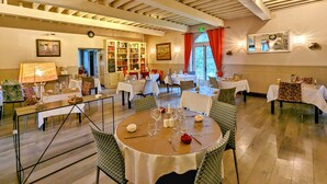A dining area with round tables, chairs, and a bookshelf. - Château Corneille (Le Val d'Hazey)