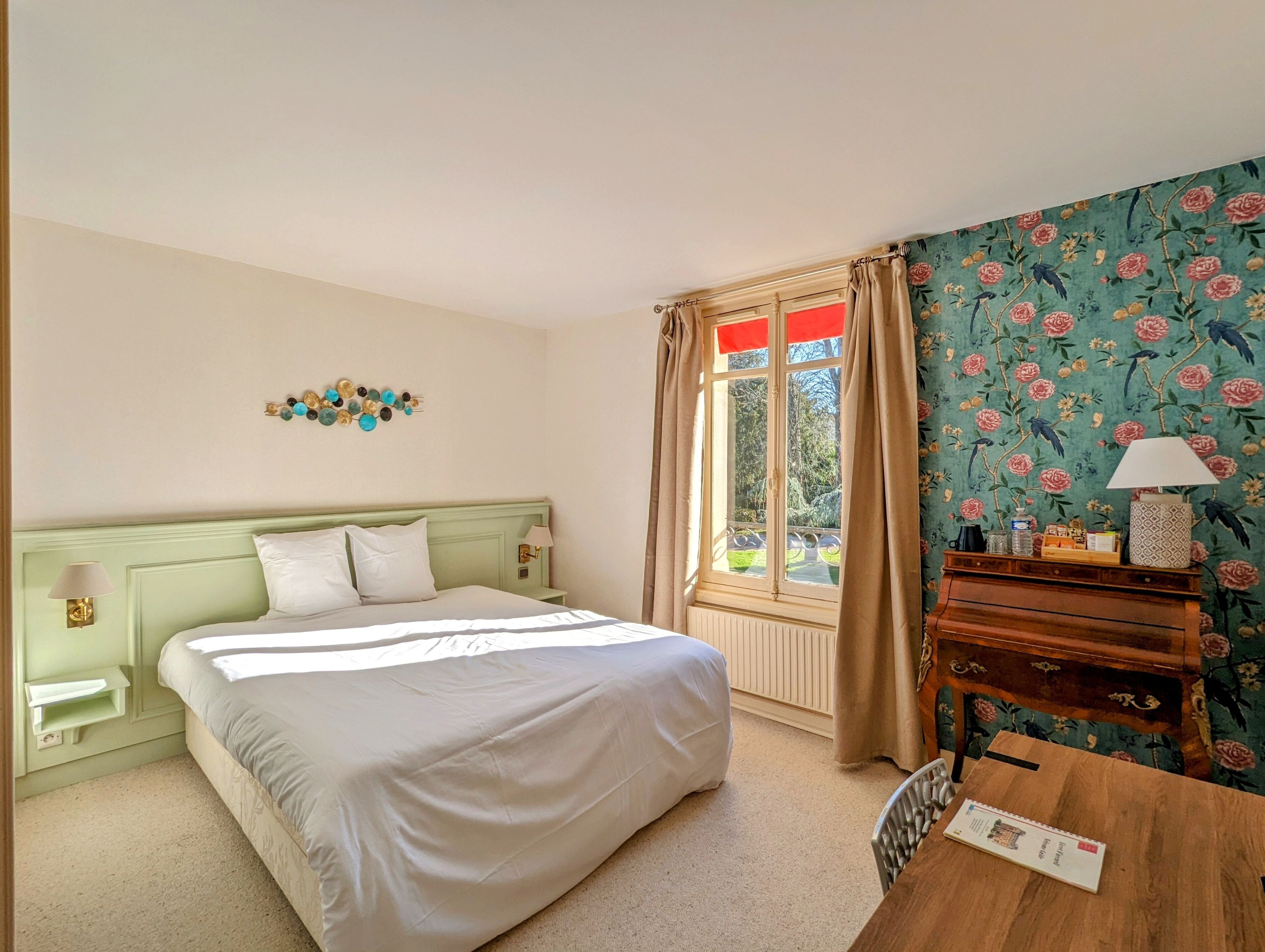 Een slaapkamer met een bed, nachtkastje, kapstok en een raam met gordijnen, en bloemenbehang.