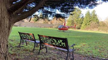 Un parco con due panchine di legno sotto un albero, un elicottero rosso sullo sfondo e un muro in pietra.