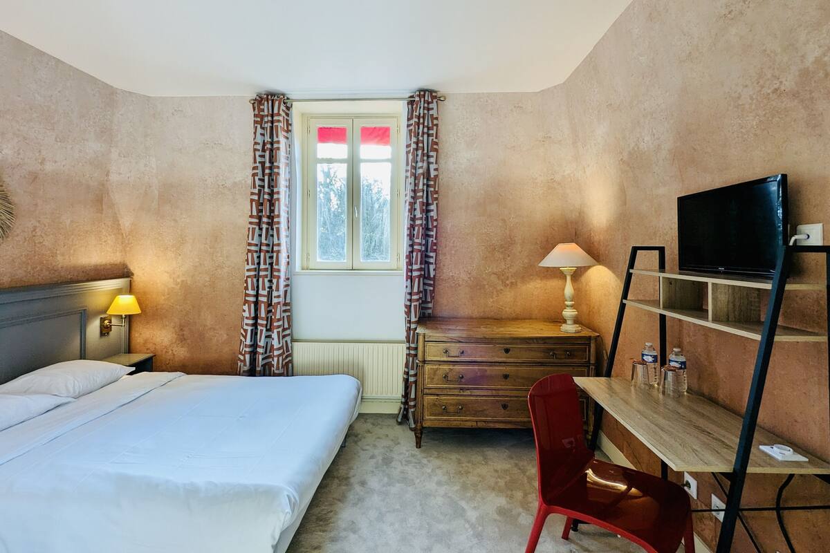 Una habitación de hotel con una cama, un escritorio con lámpara, televisión y una silla.