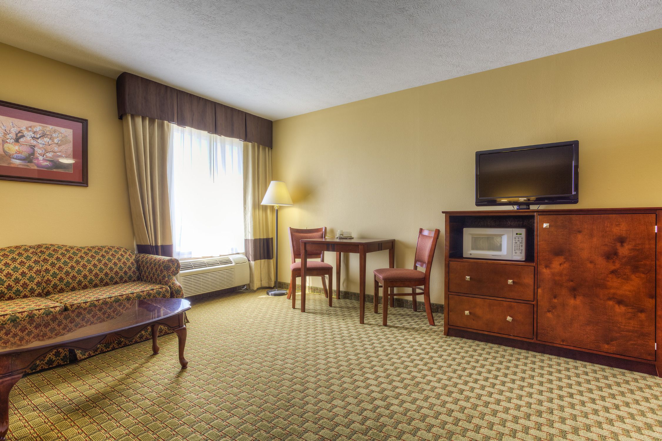 A hotel room with a sofa, a dining table with chairs, a television, a microwave, and a cabinet.