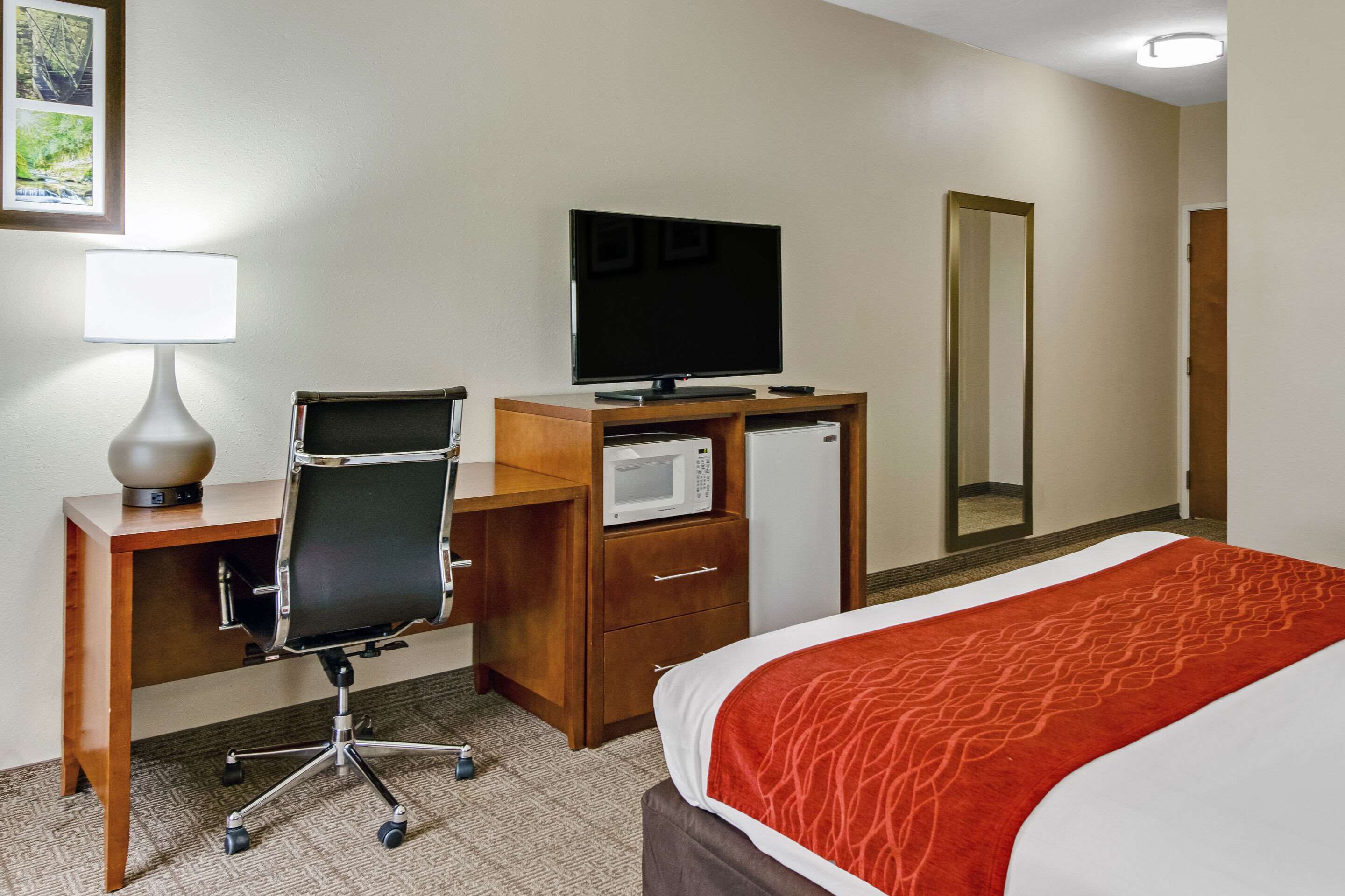 Hotelkamer met een bed, bureau, stoel, televisie, magnetron en spiegel.
