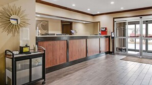A reception area with a wooden reception desk, a glass service cart, a mirror, and a glass door leading outside. - Comfort Inn Henderson - Evansville South (Henderson)