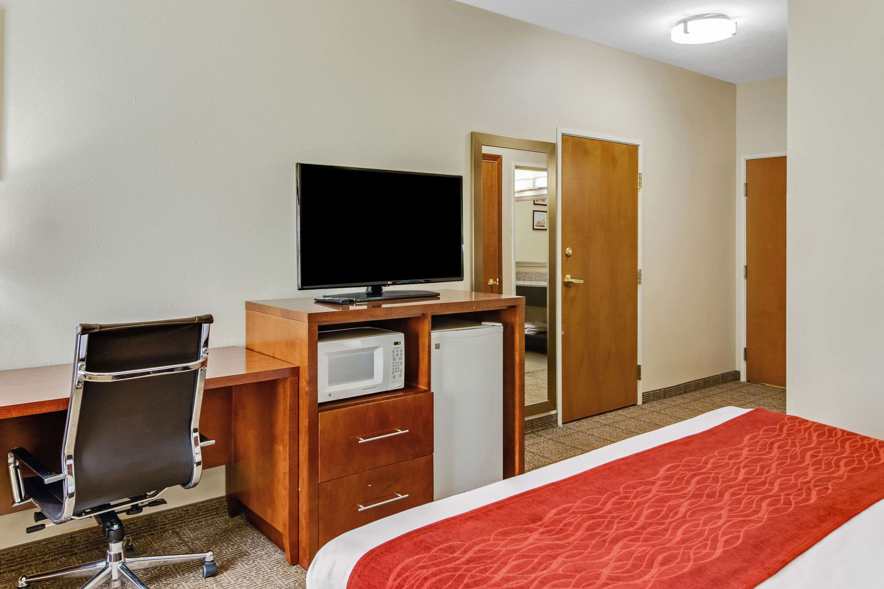 A hotel room with a bed, a desk with a computer and a television, a microwave, and a refrigerator.