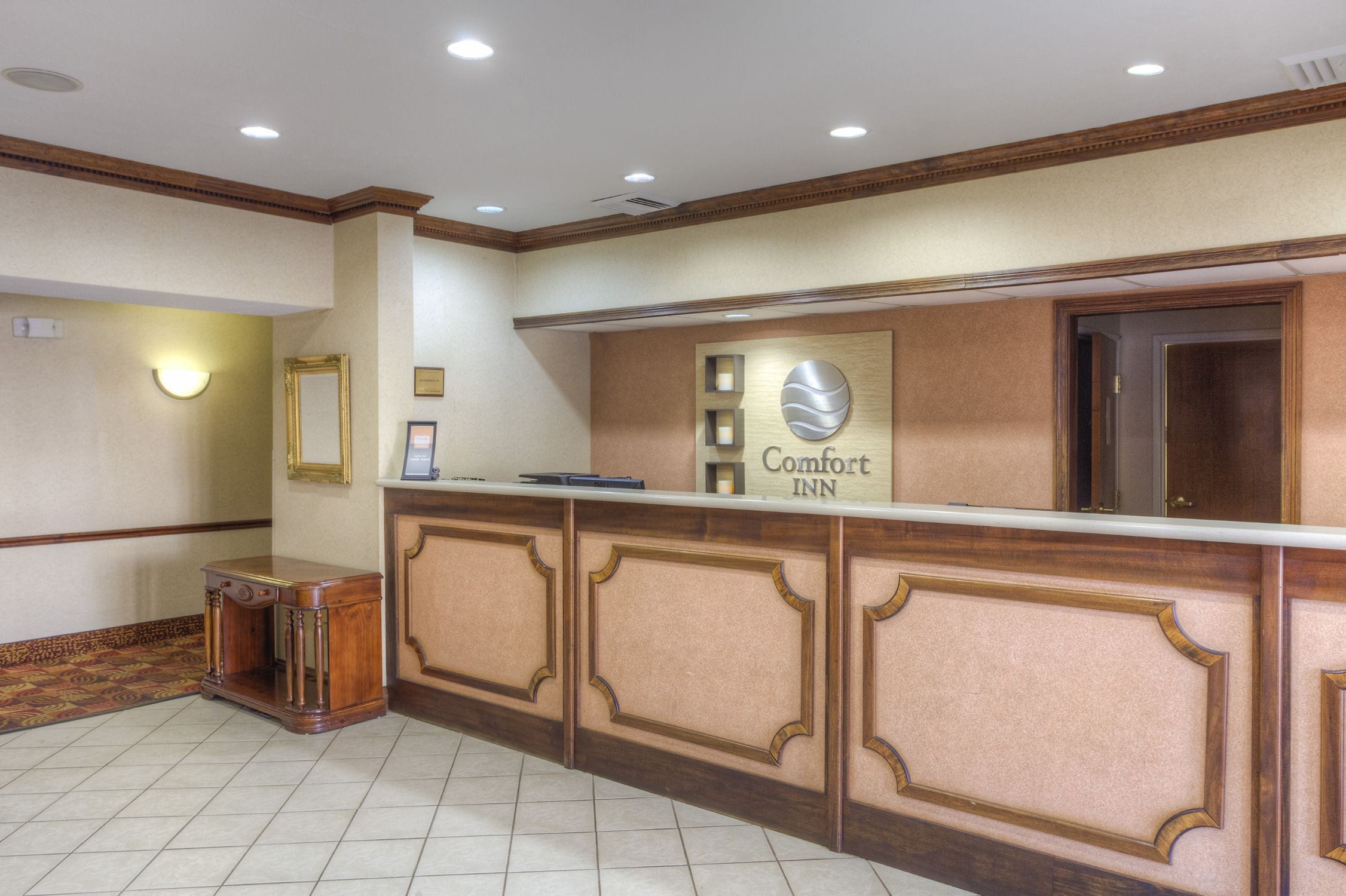 Un espace d’accueil avec un comptoir de réception en bois, une enseigne indiquant « Comfort Inn » et un tableau encadré accroché au mur.