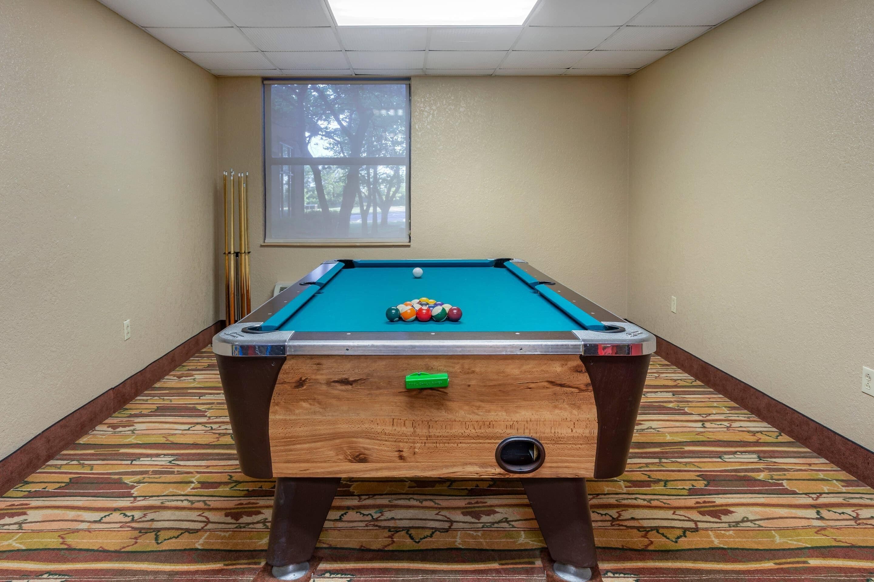 A pool table with balls, a projector screen, and a window with a view of trees.