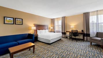 A hotel room with a bed, a desk, a chair, a sofa, and two lamps.