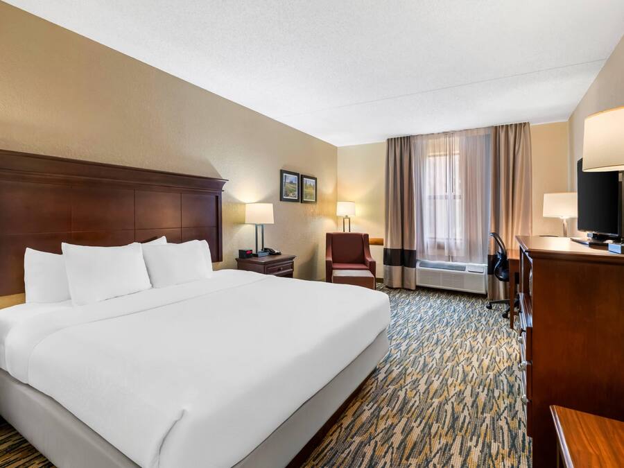 Habitación de hotel con una cama grande, un escritorio, una silla, una lámpara de escritorio, un teléfono, un televisor y una ventana con cortinas.