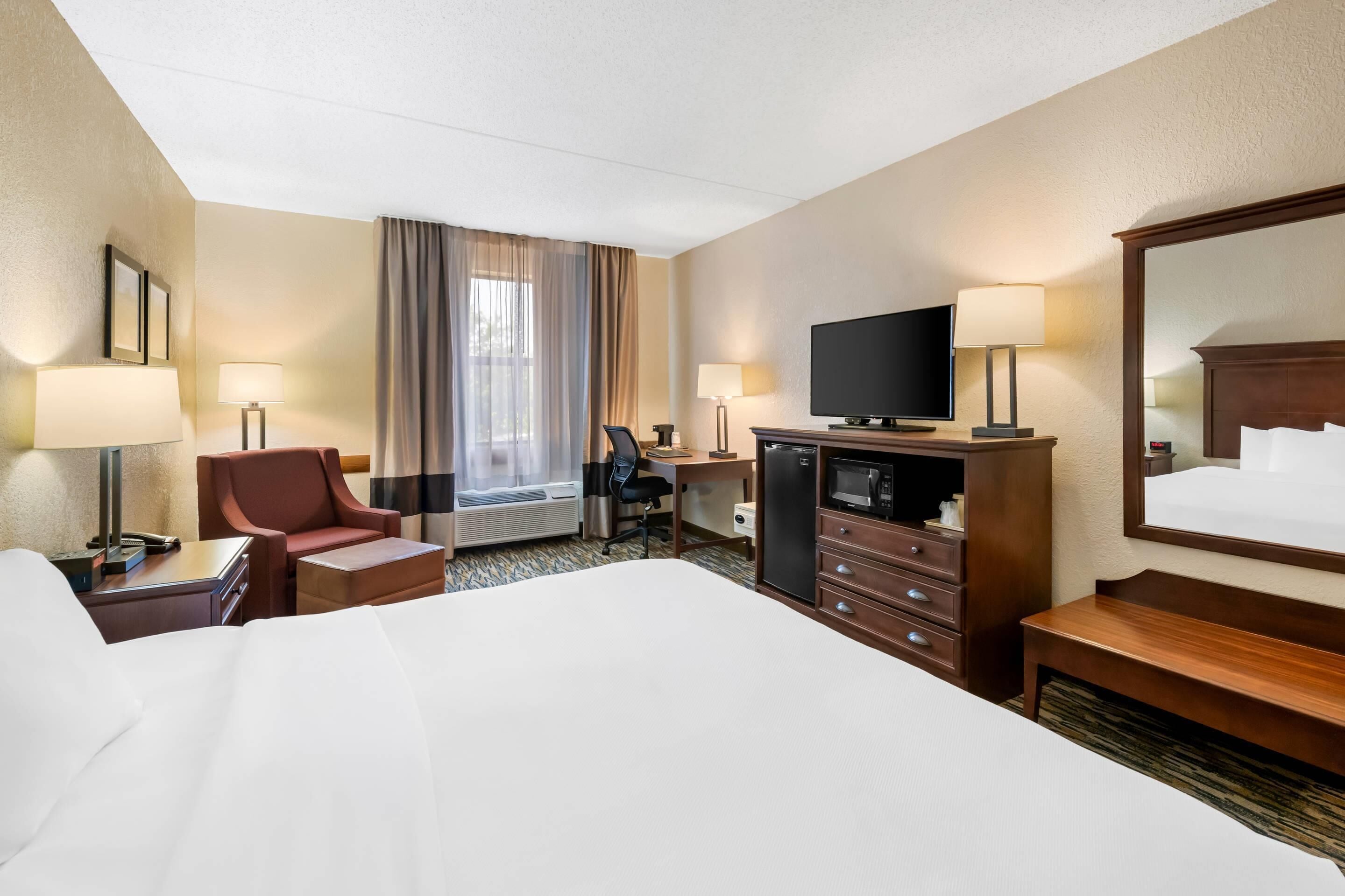 A hotel room with a large bed, a desk with a computer, a television, and a minibar.