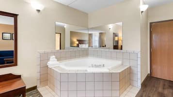 Un baño de hotel con una bañera grande, un espejo y un banco de madera.