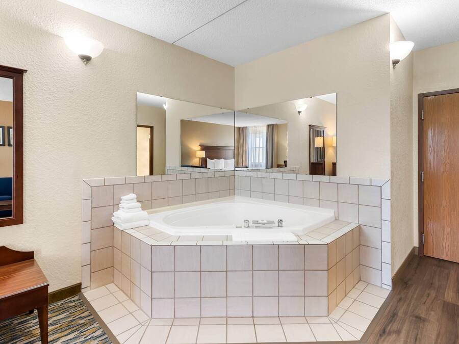 Un baño de hotel con una bañera grande, un espejo y un banco de madera.