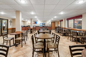 A restaurant with multiple tables and chairs, a counter area, and a tiled floor.