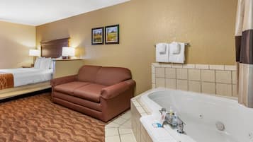 A hotel room with a bed, a sofa, a bathtub, and two framed pictures on the wall.