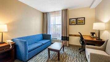Quarto de hotel com um sofá azul, uma escrivaninha de madeira, uma cadeira, um telefone e duas luminárias.