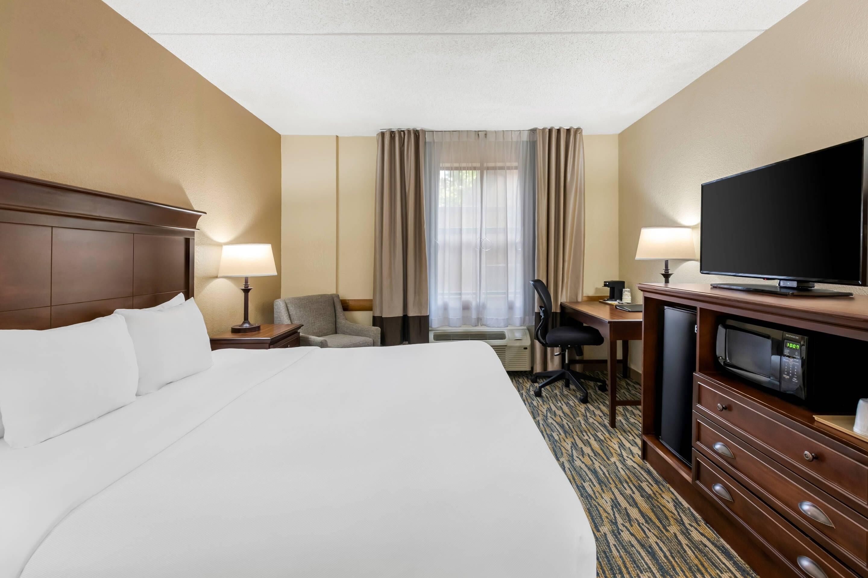 Ein Hotelzimmer mit einem großen Bett, einem Schreibtisch mit Computer, einem Fernseher und einer Minibar.