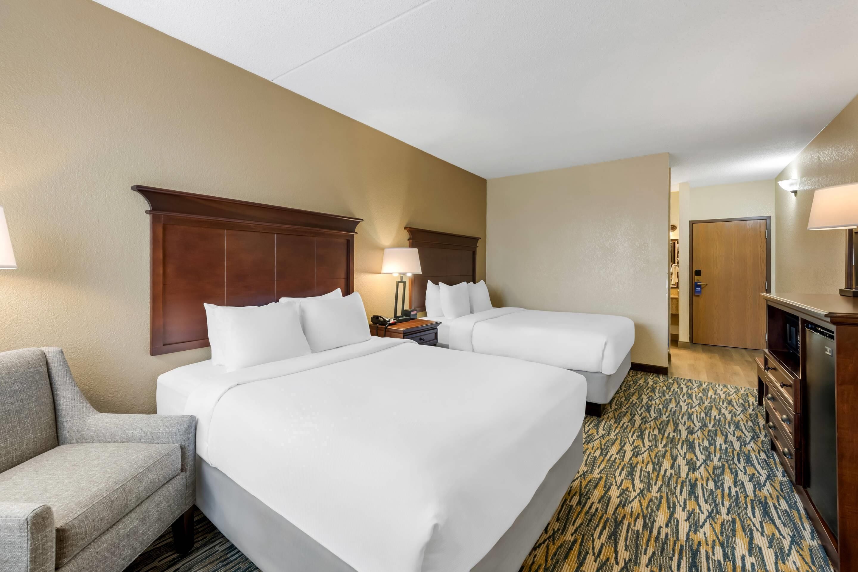 A hotel room with two beds, a desk, a chair, a lamp, and a patterned carpet.