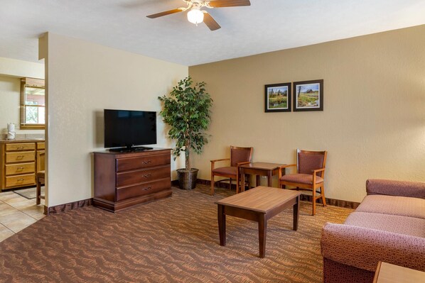 A living room with a television, a dining table, two chairs, a sofa, a ceiling fan, and a potted plant.