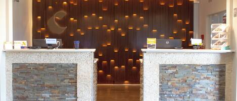 A reception area with two counters, each with a computer and a sign that reads "Welcome." The walls are adorned with a wooden panel design and recessed lighting.
