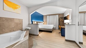 Una habitación de hotel moderna con una bañera grande, una cama, un escritorio y un espejo.