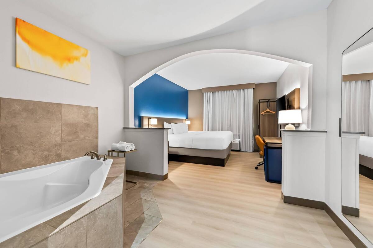 Een moderne hotelkamer met een groot bad, een bed, een bureau en een spiegel.