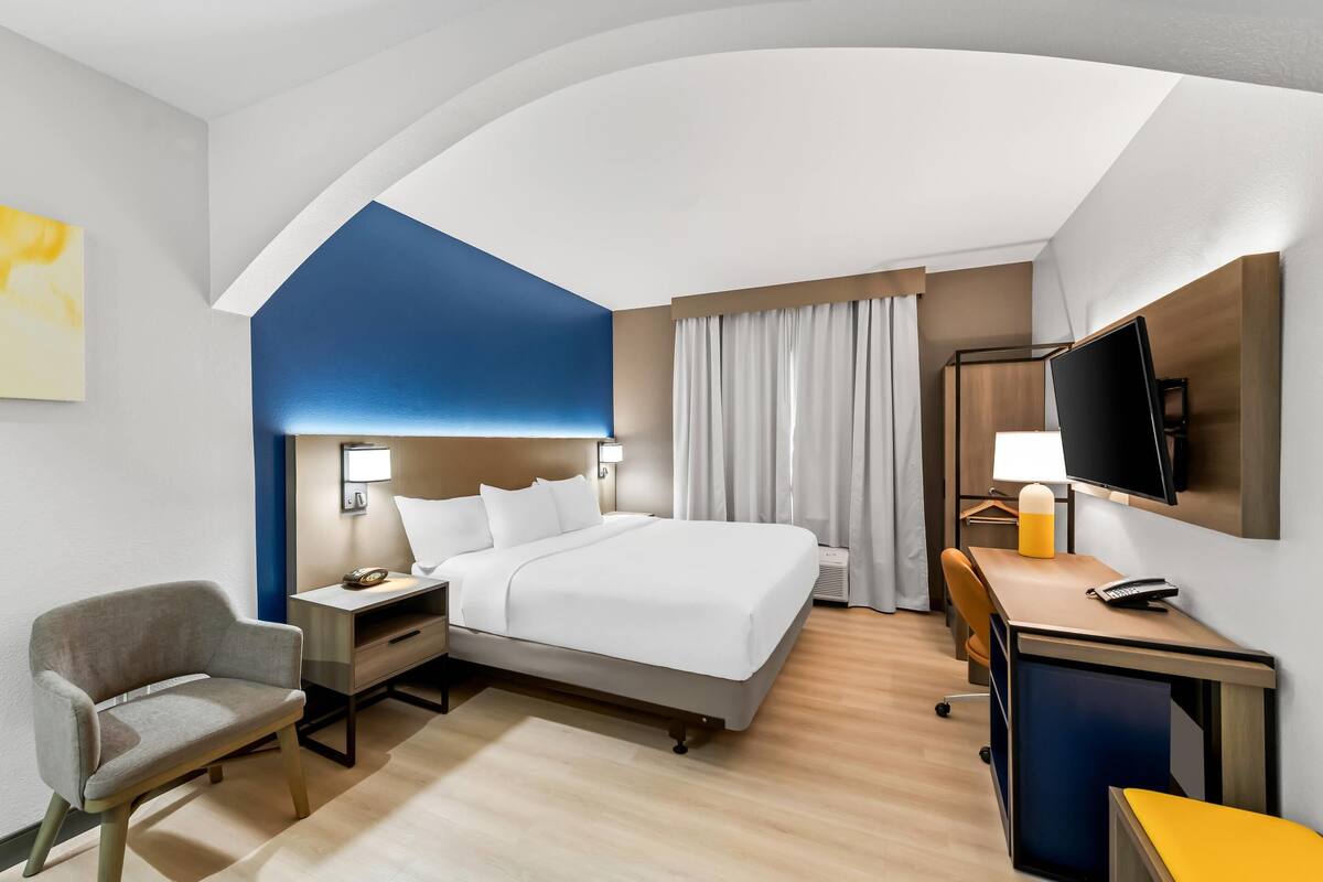 Hotelkamer met een bed, bureau, stoel, televisie en een schilderij aan de muur.