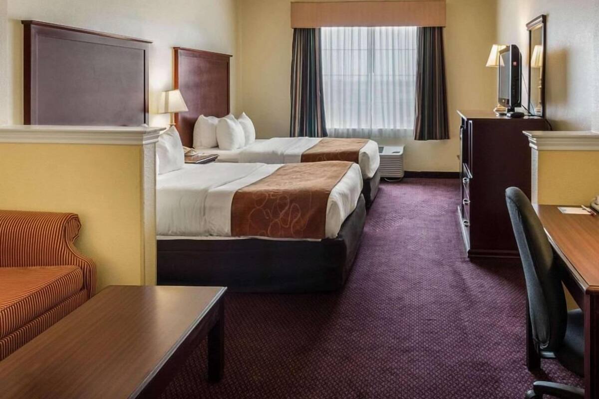 Een hotelkamer met twee bedden, een bureau, een stoel, een televisie en een raam met gordijnen.