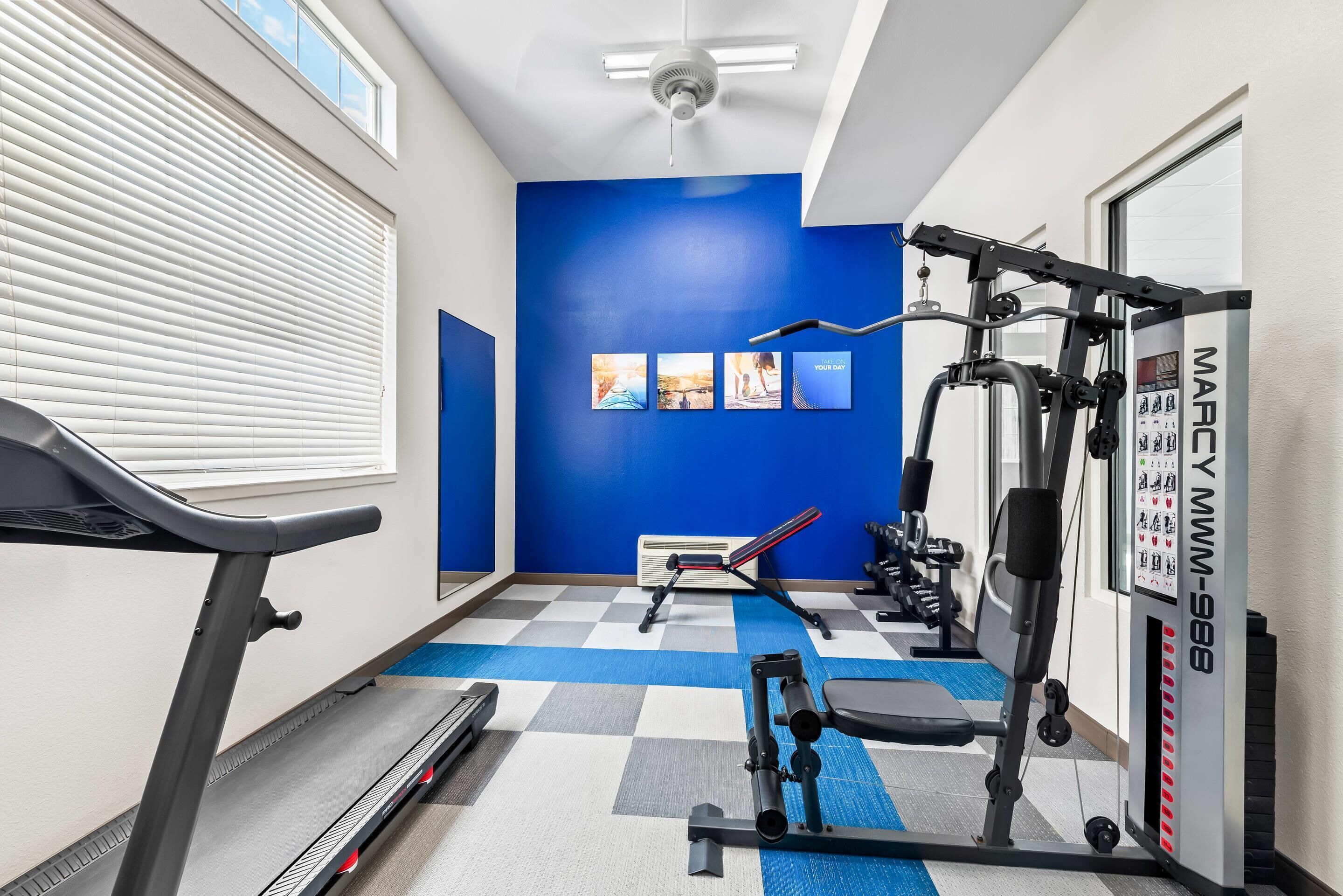 A gym with a treadmill, weight machines, and a blue wall with motivational posters.
