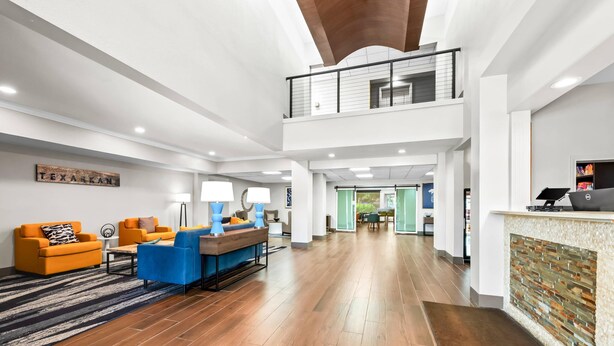 Un espacio habitable amplio con techo alto, piso de madera y una zona de estar con sofás naranja y azules.