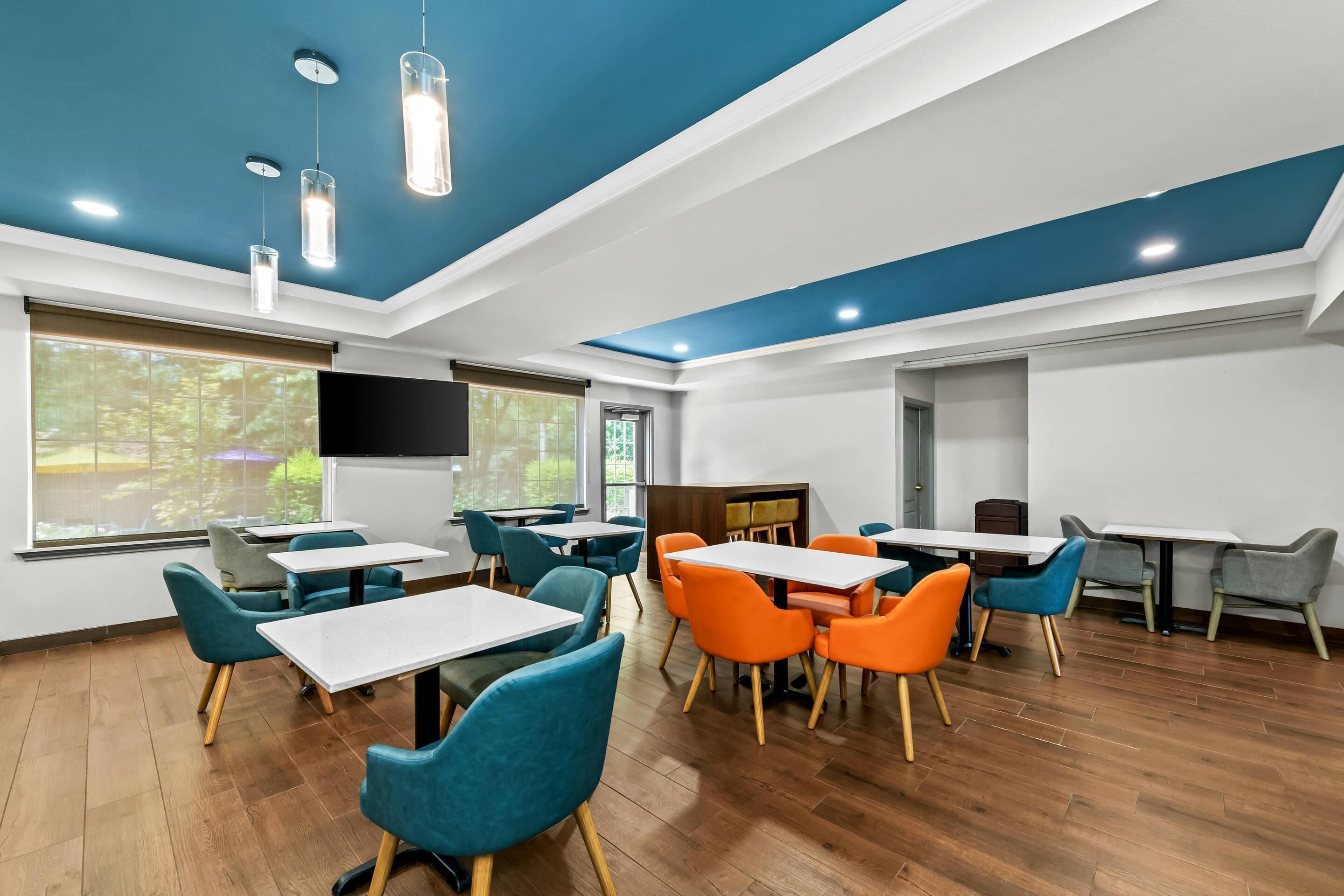 Un espace repas moderne avec un plancher en bois, des chaises bleues et oranges, et des tables.