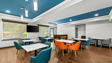 A modern dining area with wooden flooring, blue and orange chairs, and tables.