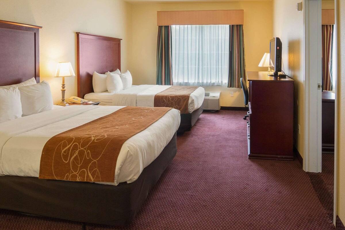 Een hotelkamer met twee bedden, een bureau, een stoel, een televisie en een raam met gordijnen.