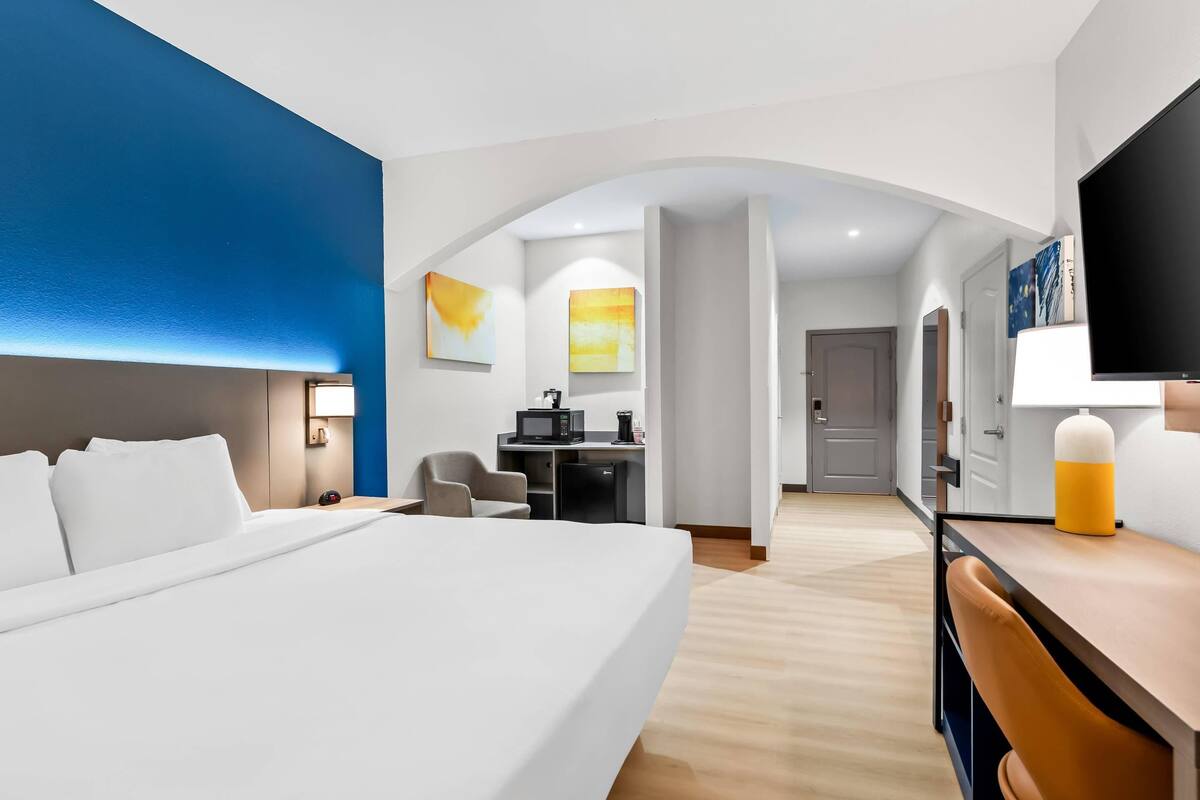 Een moderne hotelkamer met een groot bed, een bureau met een computer, een televisie en kunstwerken aan de wanden.