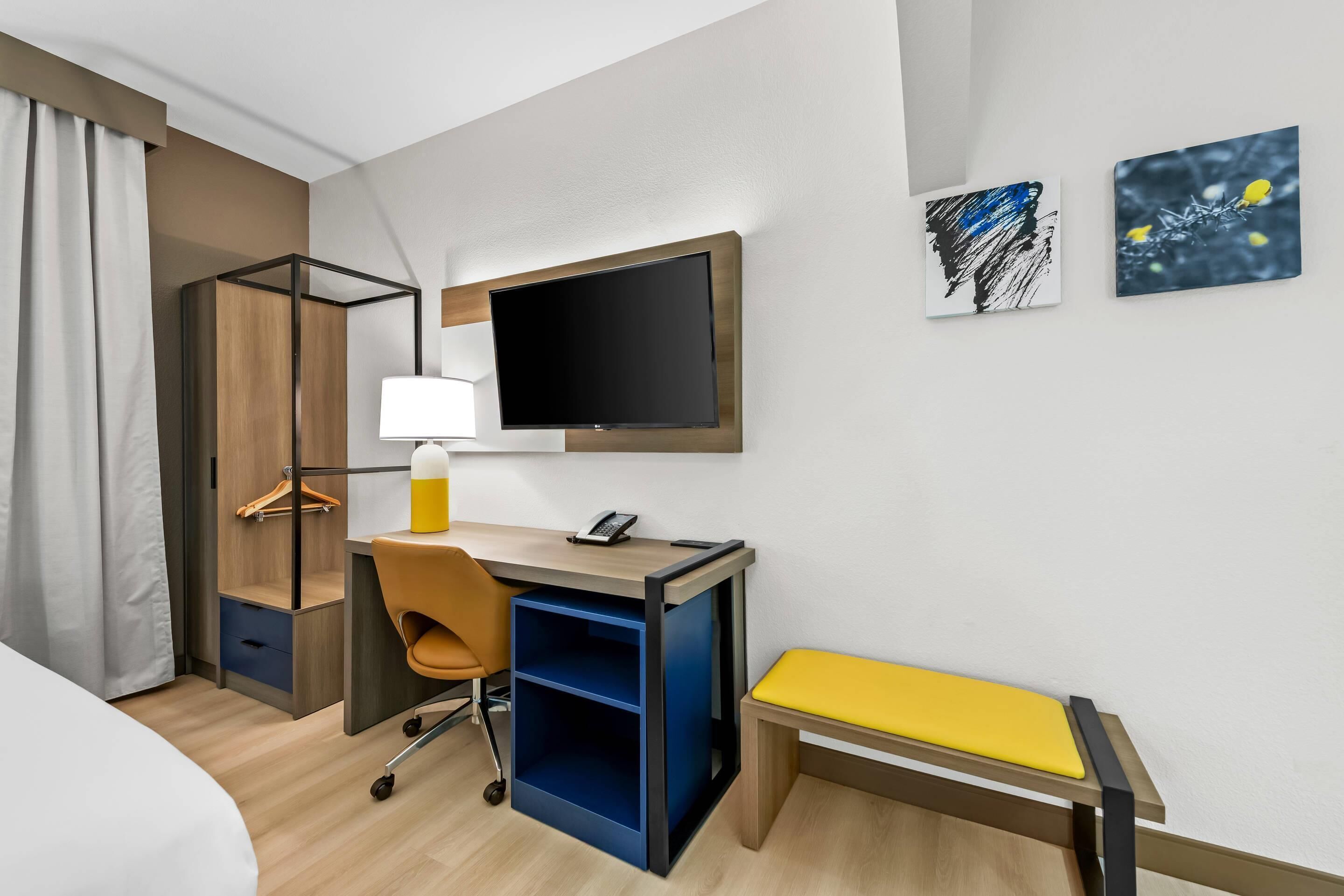 Een hotelkamer met een bed, een bureau met stoel, een televisie en twee kunstwerken aan de muur.