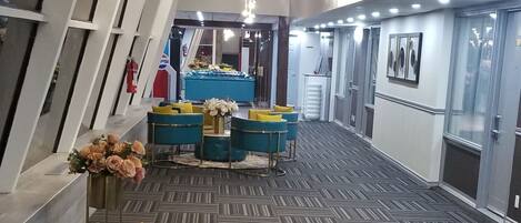 Un vestíbulo amplio con techos altos, candelabros modernos y una zona de estar con sillones amarillos y azules.